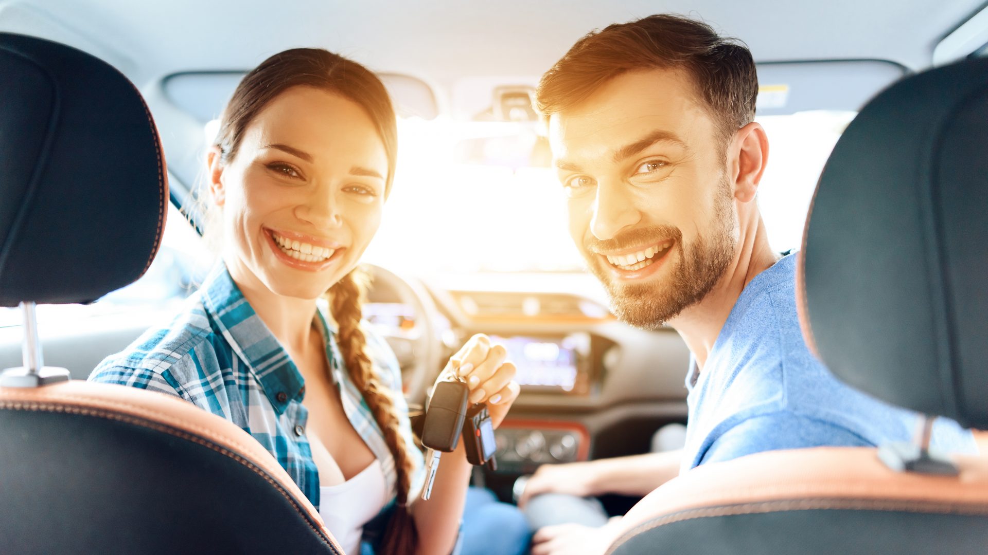 Girl and the guy are sitting in a new car and smiling.